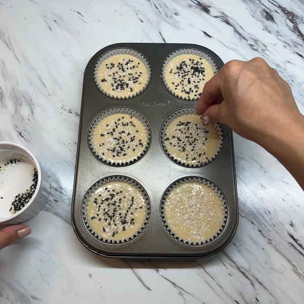 topping the mochi muffins with black sesame seeds and coconut flakes